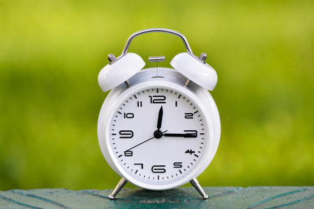 White alarm clock on green background.