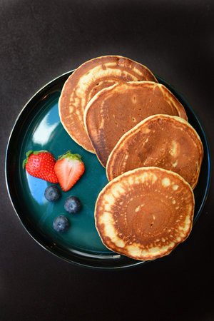 Stack of pancakes with fresh berries on a blue plate on black background