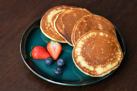 Pancakes with strawberries and blueberries on a green plate on a wooden table