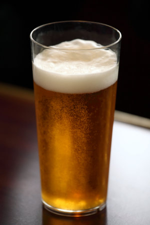 A pint of recently drawn foaming lager on a tabletop.