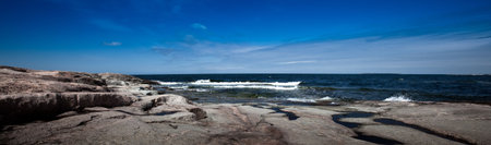 A panoramic shot of a stony island coastline on a clear summer day.