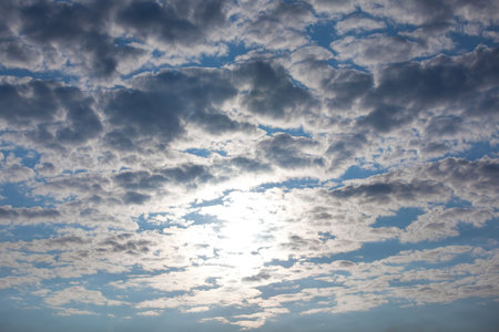 The sun shining behind clouds on a bright summer morning.