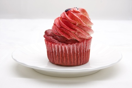 Red velvet cupcake decorated with red colored buttercream frosting on a white plate against a white background.の写真素材
