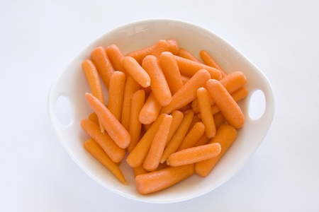White bowl of fresh, raw baby carrots against a white background.の写真素材