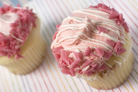 Yellow cupcakes decorated with pink frosting against a multi-colored striped background.の写真素材