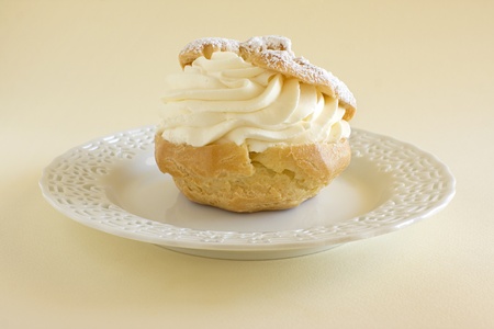 Creme puff pastry dessert on a white china plate against a yellow background.の写真素材