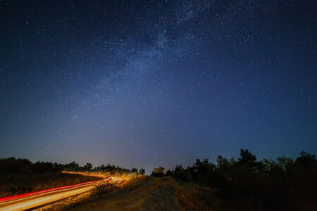 Road at night against the background of the starry sky and the Milky Way. Long exposure.の写真素材