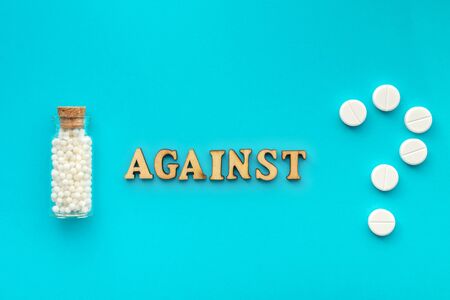 Homeopathy versus traditional medicine. From above bottle with sugar drops of homeopathy remedy against traditional medicine pills against bright blue background.の写真素材
