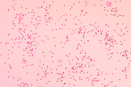 Bright pink glitter confetti on soft pink background. Festive holiday pastel backdrop. Celebration...
