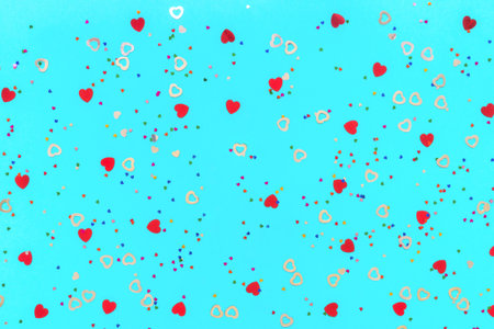 Photo of confetti in shape of heart different sizes and colors sprinkles on blue backdrop. Festive...
