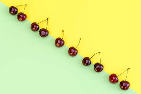 Cherry pattern. Flat lay of cherries on a pastel yellow and green background. Geometrical and minimal composition.の写真素材