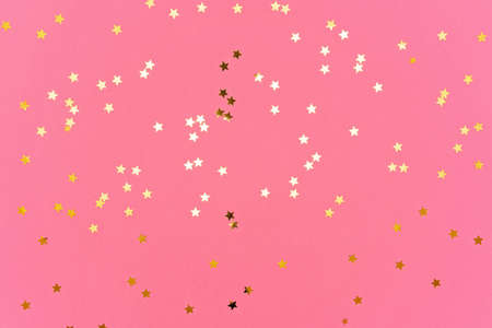 Photo of gold colored stars glitter sprinkles on pink trendy background. Festive holiday background for your projects. Celebration concept. Top view, flat lay.の写真素材