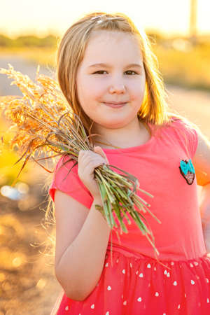 Cute smiling little girl in pink dress with bouquet of dried flowers in her arm outdor in sunset. Activities with children summer outdoors. Vertical.の写真素材