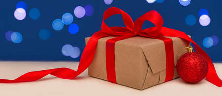 Holiday concept. Banner of christmas gift box with red bow and christmas red ball on blue bokeh background. Holiday greeting card. Copy space.の写真素材