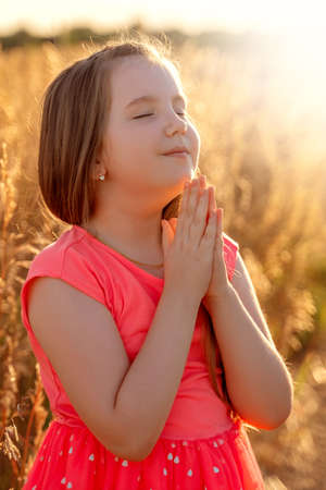 Little girl folded her hand and close your eyes in praying, dreaming in field outdoors. Child praying. Concept for faith, spirituality and religion.の写真素材