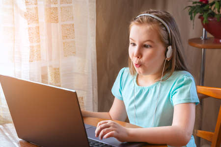 Cute little girl sitting playing on a laptop computer at home looking at the camera with a joyful expression of amazement and wonder. She get social media notification scream wow omg.の写真素材