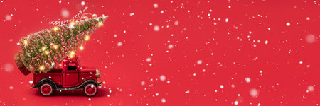 Banner photo of red small retro toy truck with sparkling Christmas tree lights on truck body on red...