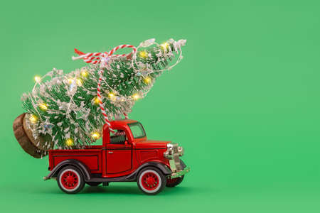 Red small retro toy truck with sparkling Christmas tree lights on truck body on green background. Delivery. Christmas, New Year concept. Front view, copy space.の写真素材