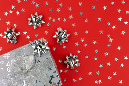 Beautiful silver box gift present with many silver ribbon bows on a red background for Christmas,...