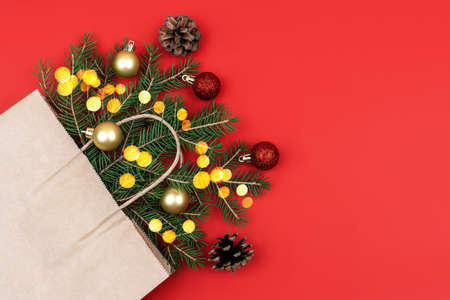 Festive Christmas composition with fir branches into craft package and christmas balls against red background and golden bokeh. Eco-friendly packaging in kraft paper. Flat lay, copy space, mock upの写真素材