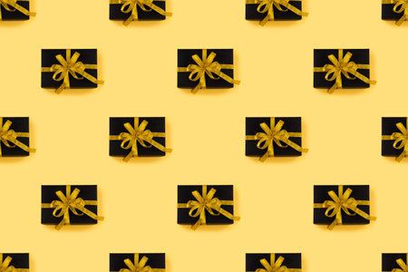 Seamless pattern of beautiful black box gift present with golden ribbon bow against golden backgroundの写真素材