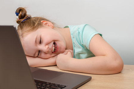 Distance learning online education. Laughing little girl using a laptop and speack via internet with...