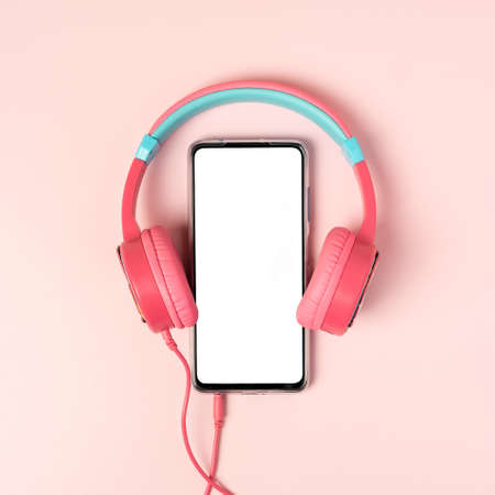 A top view on the smartphone with white screen and earphones on pink background. Studio shot concept about communication and music. Mock up template, flat lay, copy space.の写真素材