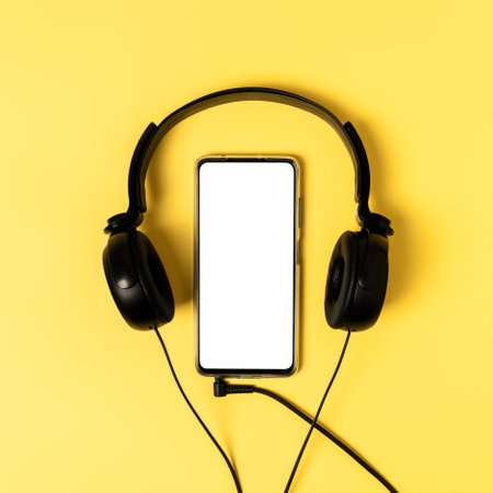 A top view on the smartphone with white screen and earphones on yellow background. Trendy color of 2021. Top view, flat lay.の写真素材