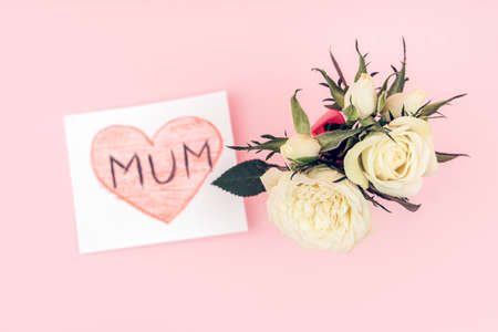 A gift from a child for mothers day - a hand made card with white rose flowers on pink background. Flat lay, top view.の写真素材