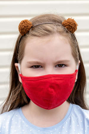 Close up photo of pretty child looking into camera wear red breathing reusable mask. She is angry and furrowed her eyebrows. Coronavirus Covid-19 and Air pollution concept.の写真素材