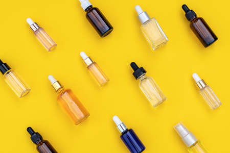 Abstract pattern of serums in glass bottles with dropper on bright yellow background. Creative layout, cosmetic pattern, flat lay. For packaging design, printing on fabric, paperの写真素材