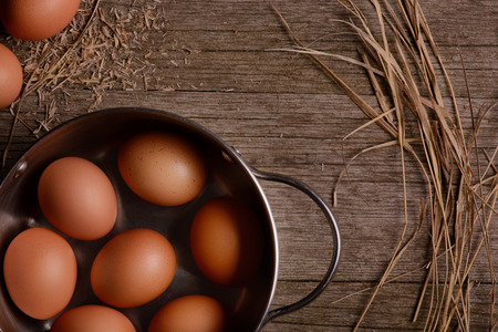 chicken eggs in pan on rustic wooden background with strawの写真素材