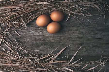 chicken eggs in pan on old rustic wooden table background with strawの写真素材
