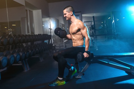 Closeup portrait of young muscular man workout with dumbbells at gym. Sport, workout.の写真素材