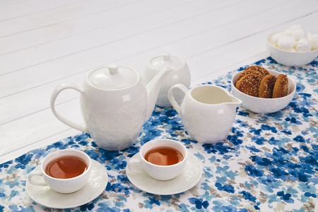 cups of tea with milk, cream and biscuits on wooden white tableの写真素材