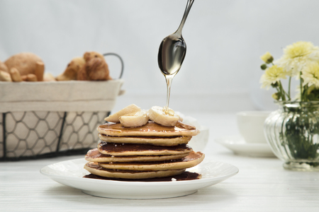Woman pouring honey onto tasty pancakes with bananas on table, closeupの写真素材