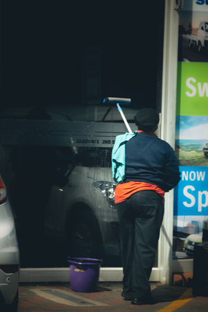 Johannesburg , Gauteng / South Africa - October 20 2018 :  african woman using a squeegee to clean a window midday rosettenville johannesburgのeditorial素材