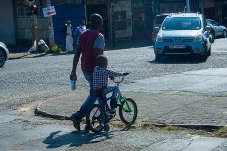 Johannesburg , Gauteng  South Africa - May 30 2022 : father helping his son across the road with his bicycle late morning rosettenville johannesburgのeditorial素材