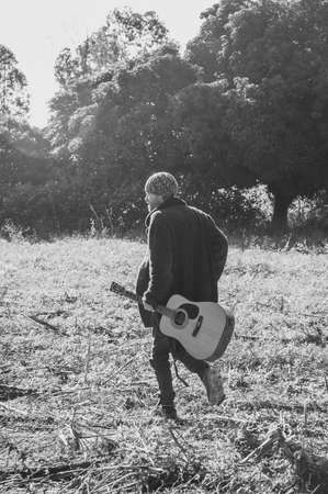 Young man playing guitar in a field. Black and white photo.の写真素材