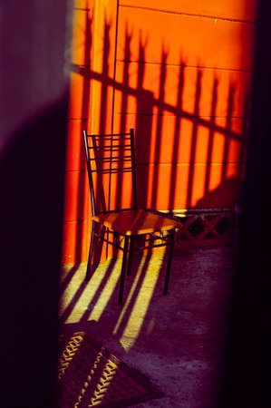 A vertical shot of a chair in front of an orange wall with shadowの写真素材