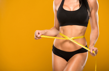 beautiful fitness model measures the waist on a yellow backgroundの写真素材