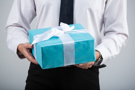 Portrait of a businessman with a gift box on a gray backgroundの写真素材