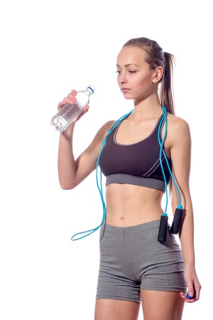 Fitness woman in sports style with a rope drinks water while standing on a white backgroundの写真素材