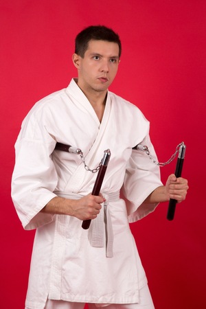fighter in white kimono with nunchaku training on a red backgroundの写真素材