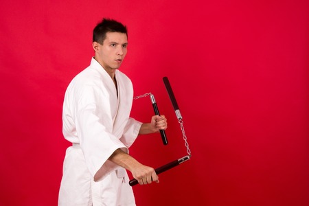 fighter in white kimono with nunchaku training on a red backgroundの写真素材
