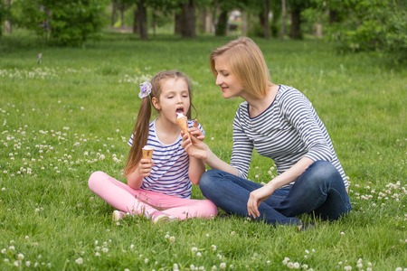 happy mother and daughter eating ice cream while sitting on the grass in the parkの写真素材