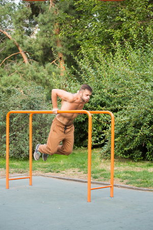 fitness, sport, exercising, training and lifestyle concept - young man doing triceps dip on parallel bars outdoorsの写真素材