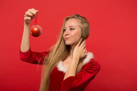 Girl dressed as Santa with Christmas and New Year tree toys on a red background.の写真素材