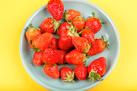 Fresh strawberry in a blue cup on a yellow background.の写真素材