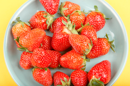 Fresh strawberry in a blue cup on a yellow background.の写真素材